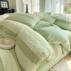 a bed covered in green pillows and blankets with a white dog bowl on the side