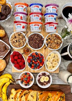 an assortment of breakfast foods laid out on a wooden cutting board with yogurt, granola, fruit, and chocolate