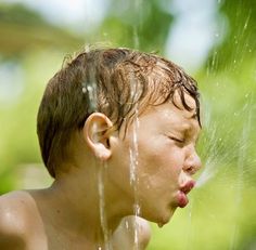 a young boy drinking water out of a sprinkler with his face close to the ground