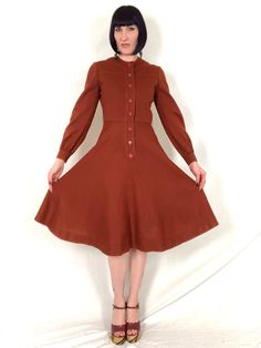 "Vintage 1970's OSCAR de la RENTA Pumpkin Spice Latte Knit Fit and Flare Balloon Sleeve Dress! Features: - balloon sleeves that gather at cuffs with a single button each - fitted bodice with yoke - nipped in waist - flared skirt - 8 matching buttons down front for closure - pumpkin spice latte / orange-brown - no fabric content labels, but feels like a tight knit acrylic Label: \"Oscar de la Renta Boutique\" Bust: up to 36\" Waist: 26\"- 27\" Hips: free Length: 42\" Model is 5' 9\" and measures Retro A-line Vintage Dress For Fall, Vintage A-line Midi Dress For Fall, Retro A-line Midi Dress For Fall, Retro Brown Midi Dress, Retro Winter Daywear Dresses, Retro Winter Day Dresses, Vintage A-line Midi Dress For Winter, Retro Midi Dress For Fall, Retro Brown Dress For Fall