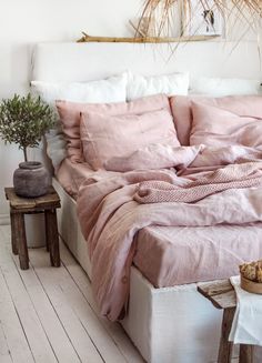 a bed with pink linens and pillows in a white room next to a potted plant