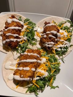 three tacos with chicken, cheese and lettuce on them sitting on a white plate