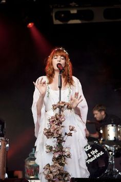 a woman with red hair wearing a white dress and holding a microphone in her hand