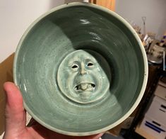 a hand holding a green bowl with a face on it's front and bottom