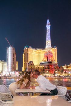 a man and woman sitting at a table in front of the eiffel tower