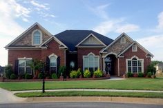 a large brick house sitting in the middle of a lush green field next to a street