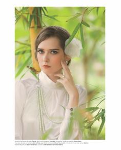 a woman in white is posing for the camera with her hand near her face and green leaves behind her