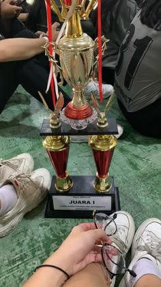 two people sitting on the floor next to a trophy with red and gold cups in front of them