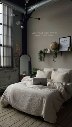 a laptop computer sitting on top of a white bed in a room with high ceilings