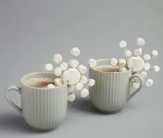 two cups with white flowers in them sitting next to each other on a gray surface