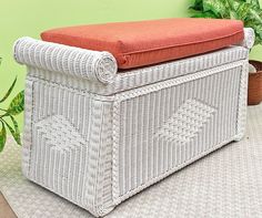 a white wicker bench with an orange cushion on it next to a potted plant