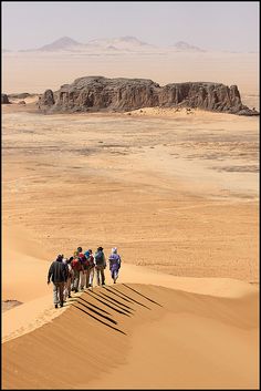 a group of people walking in the desert with sand dunes and mountains in the background