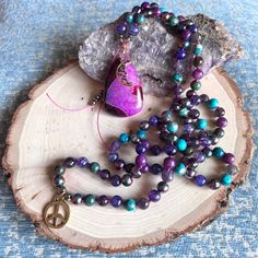 This Hand Knotted 108 Beads Mala Necklace is Made with the Following Gemstones and Crystals: Amethyst, Chrysocolla, Lepidolite, Sea Sediment Jasper, Dragon Vein Agate, Rainbow Hematite, and Finished with a Purple and Fuschia Banded Agate Pendant with Peace Sign and Crescent Moon Charms. Tranquil and protective energy exude from this beautiful Moon Inspired 108 Beads Mala Necklace. Like the moon and its many phases, our hearts, bodies, and minds can draw inspiration from flowing effortlessly with Purple Agate Bohemian Beaded Necklaces, Purple Agate Gemstone Beaded Necklace, Spiritual Purple Beaded Crystal Necklaces, Purple Beaded Spiritual Crystal Necklaces, Healing Amethyst Beaded Necklaces With Polished Beads, Healing Amethyst Beaded Necklace With Polished Beads, Handmade Purple Agate Beaded Necklaces, Handmade Purple Beaded Necklaces For Meditation, Purple Beaded Crystal Necklace For Meditation