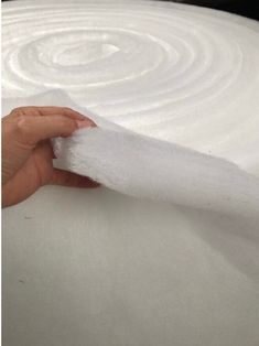 a hand is holding a piece of white paper near a roll of fabric that has been rolled up