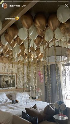 balloons are hanging from the ceiling above a bed in a room with white and gold decor