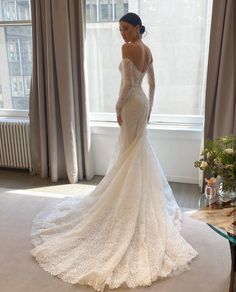 a woman in a wedding dress standing by a window with her hands on her hips