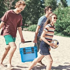 three people are walking on the beach with a cooler and ball in their hand,