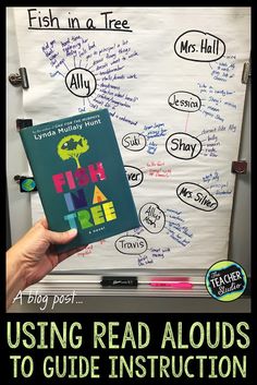 a person holding up a book in front of a whiteboard