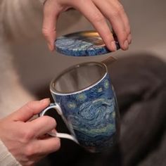 a person is holding a coffee mug with the starry night painting on it while sitting down