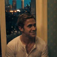 a man sitting in front of a window with the city lights lit up behind him