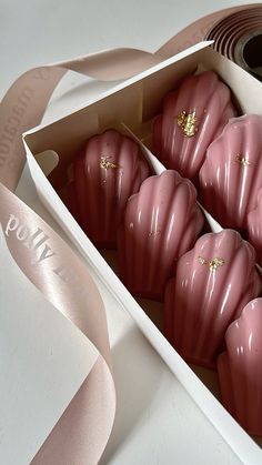 some pink chocolates in a white box on a table next to a roll of ribbon