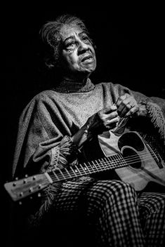 a black and white photo of a woman playing an acoustic guitar in the dark with her eyes closed