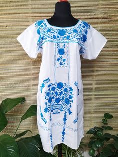 a white dress with blue flowers on it and a plant in the corner next to it