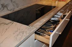 an open drawer in the middle of a counter with utensils and other kitchen items