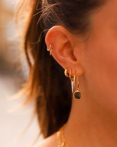 a close up of a woman's ear wearing gold earrings and a black necklace