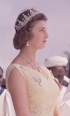 an old photo of a woman wearing a tiara and standing in front of other people