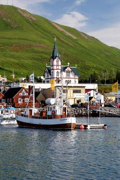 a large boat floating on top of a body of water next to a green hillside