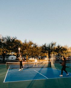 three people are playing tennis on a blue court with trees in the backround