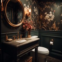 a bathroom with floral wallpaper and wooden vanity, gold faucet, white toilet and sink