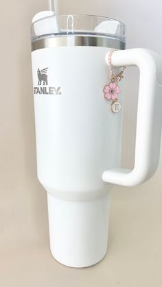 a white coffee cup with a pink flower charm on the side and a straw in it