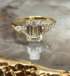 an emerald cut diamond ring with three side stones on the band, sitting on a marble surface