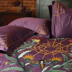 a bed covered in purple sheets and pillows with spider webs on the pillow cases