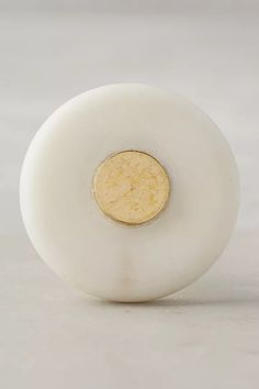 a round white object with a gold disc on the top and bottom part, sitting on a plain surface