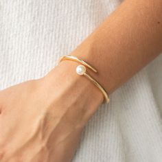 Featuring a solitaire white pearl, two shiny gold bars attach to a spring-like fitting as they curl around the wrist for a modern finish.

Sold as one individual bracelet. Modern Gold Pearl Bracelet, Modern Gold Pearl Bracelets, Rings Brand, Pearl Bangle Bracelet, Gold Bracelet Simple, Pearl Bracelet Gold, Pearl Jewelry Design, Gold Bars, Modern Bracelets