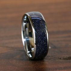 a wedding ring with blue glitter inlays on it sitting on a wooden surface