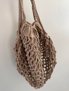 a crocheted bag hanging from a hook on a wall with white walls in the background