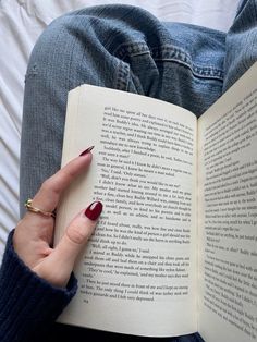 a woman with red nails is reading a book on her lap and holding it in her hand