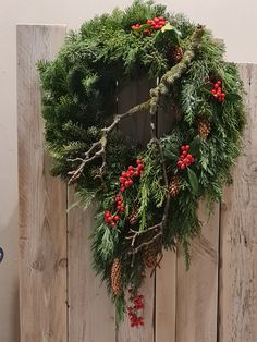 a wreath is hanging on the side of a wooden fence with red berries and pine cones