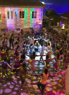 a group of people dancing in front of a building at night with lights on the ground