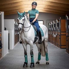 a woman riding on the back of a white horse in an indoor area with wooden ceiling