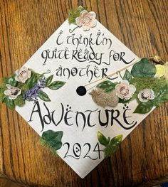 a decorated graduation cap on top of a wooden table with writing and flowers around it