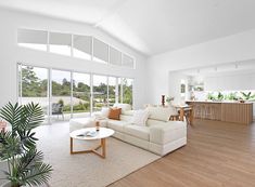 a living room filled with white furniture and lots of windows next to a wooden floor