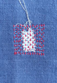 a blue piece of cloth with red and white stitching on it that has a square shaped object in the middle