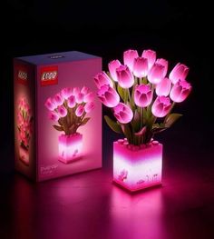 a lit up flower pot with pink tulips in it next to a box