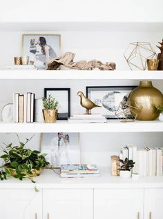 white shelves with gold vases, books and pictures on them in a living room