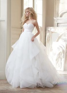 a woman in a white wedding dress standing next to a window with her hand on her hip